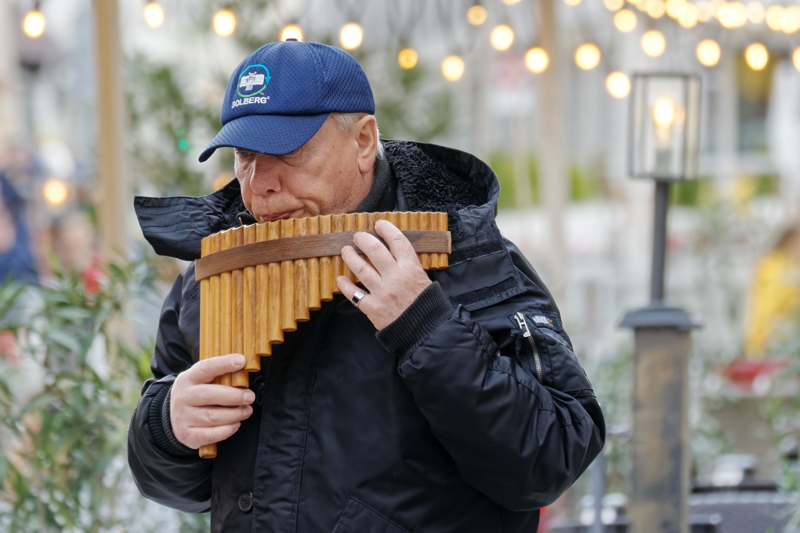 12 - An elderly street musician playing a traditional wooden pan flute